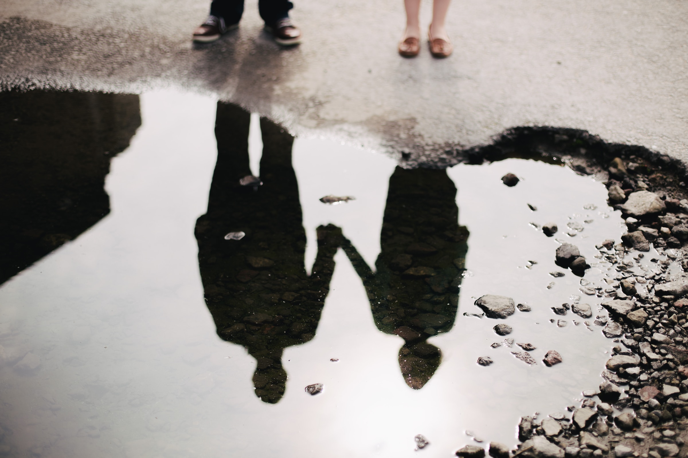 The reflection of two people standing near water holding hands.